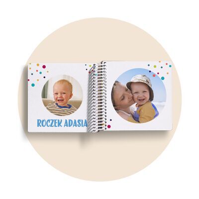 Otwarta fotoksiążka dla dzieci na spirali, z kolorowymi kropkami. Po lewej zdjęcie Adasia, po prawej z mamą. Napis: Roczek Adasia.